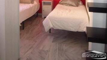 A small, compact room with two beds, a nightstand, and a red accent wall.