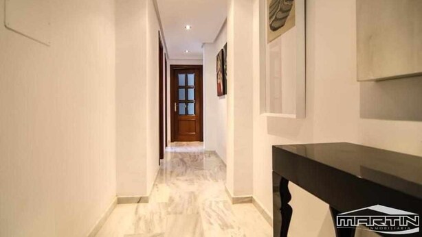 A hallway with a marble floor, a wooden door at the end, and a black console table with a logo. - APARTMENT QUINTANA CENTER (Jauja)