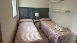 A bedroom with two beds, a bedside table with a lamp, a window, and a hanging light fixture. - APARTMENT QUINTANA CENTER (Jauja)