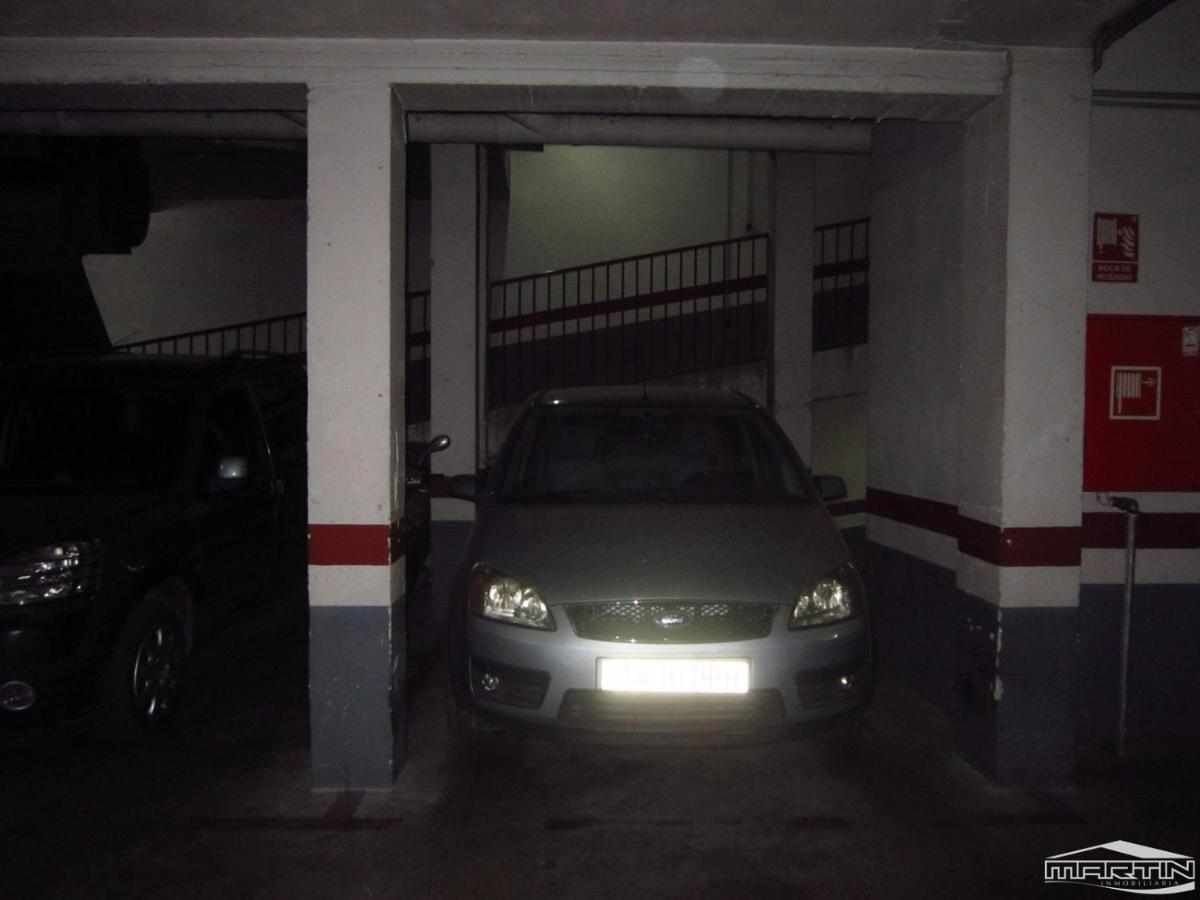 Ein Auto steht in einer schlecht beleuchteten Tiefgarage zwischen Betonpfeilern und an einem Metallgeländer.