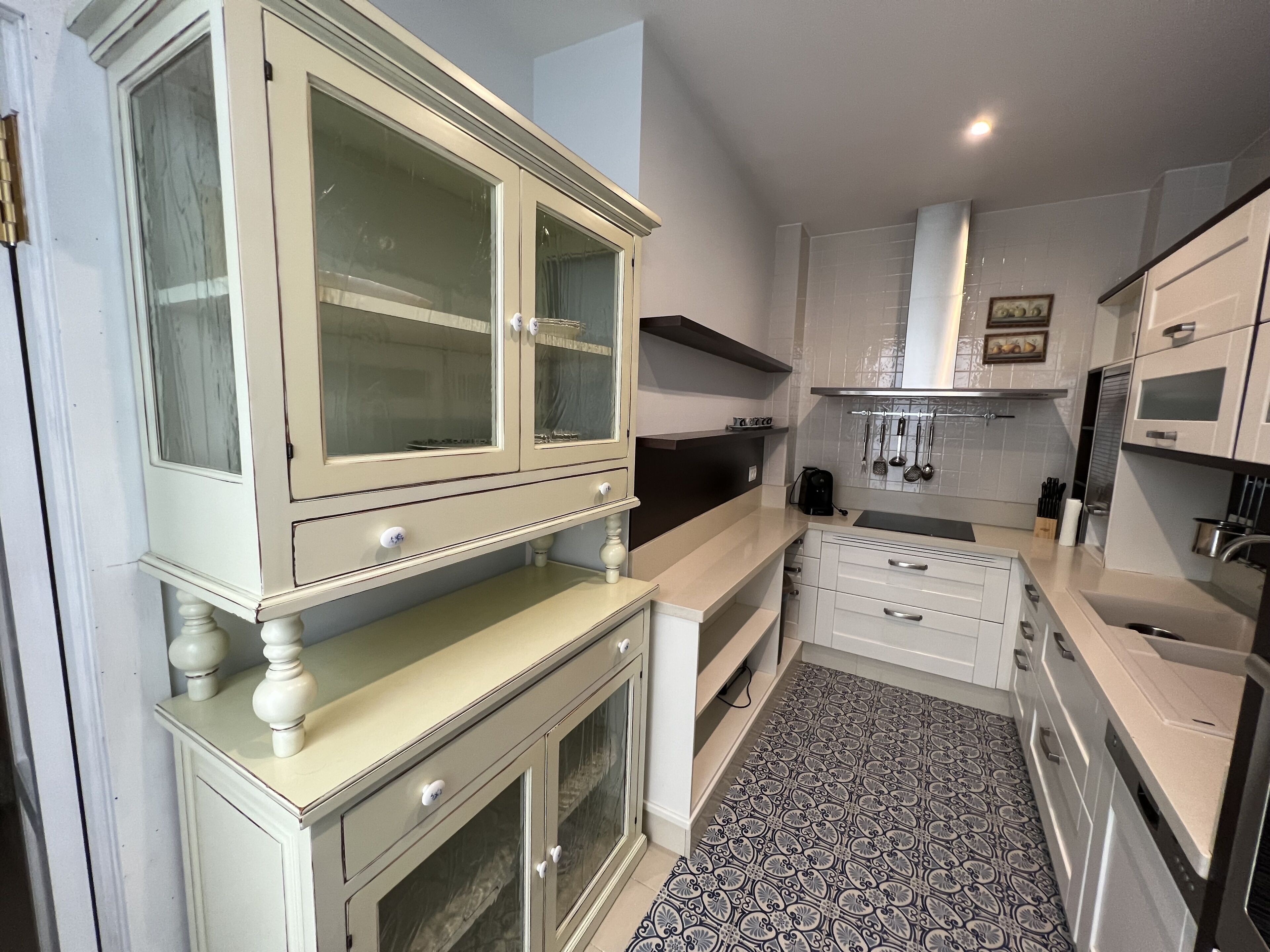 Une cuisine compacte avec des meubles blancs, une cuisinière encastrée et un crédence décorée.