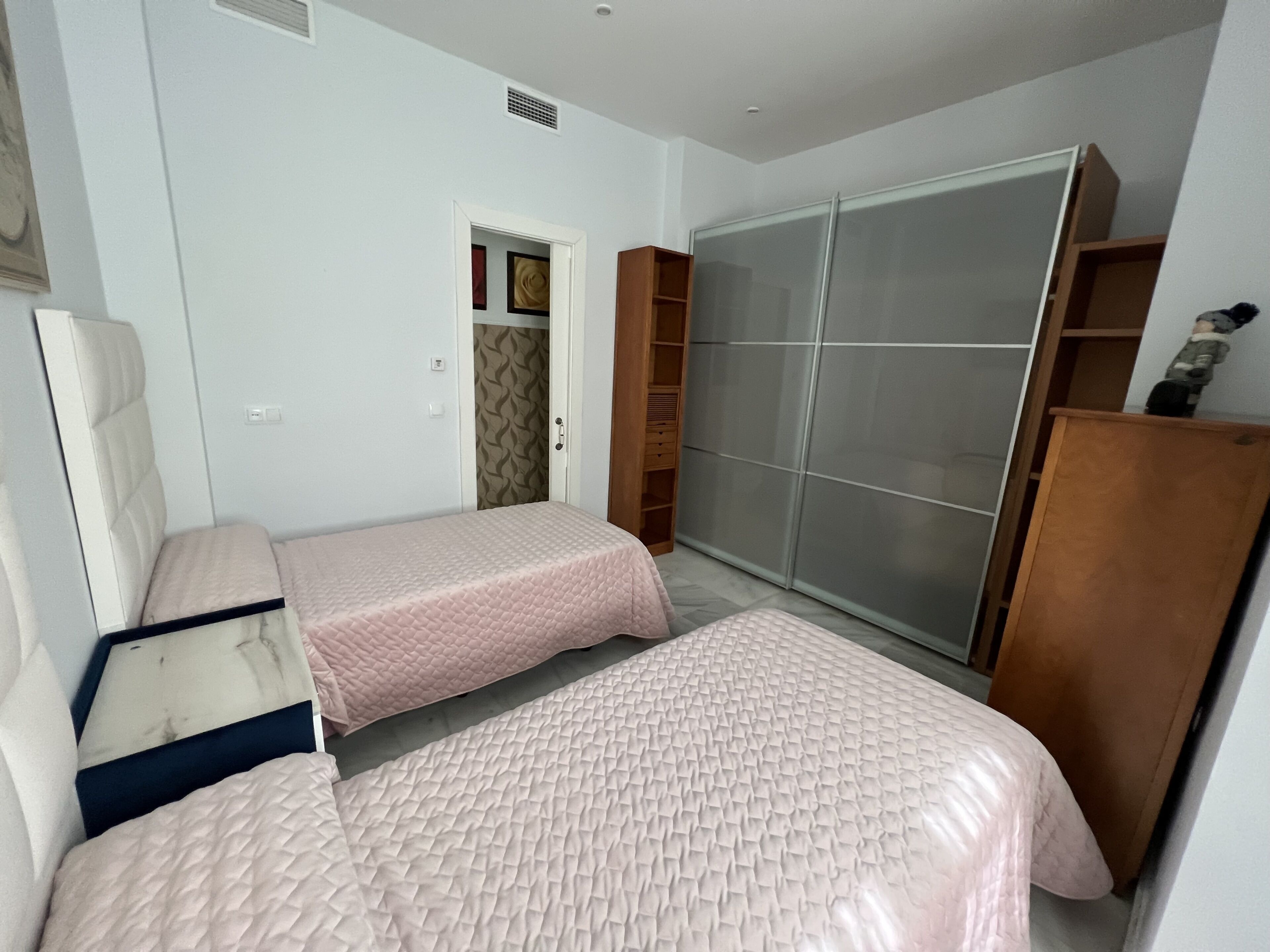 Un dormitorio con dos camas, un armario y una puerta que da a otra habitación.