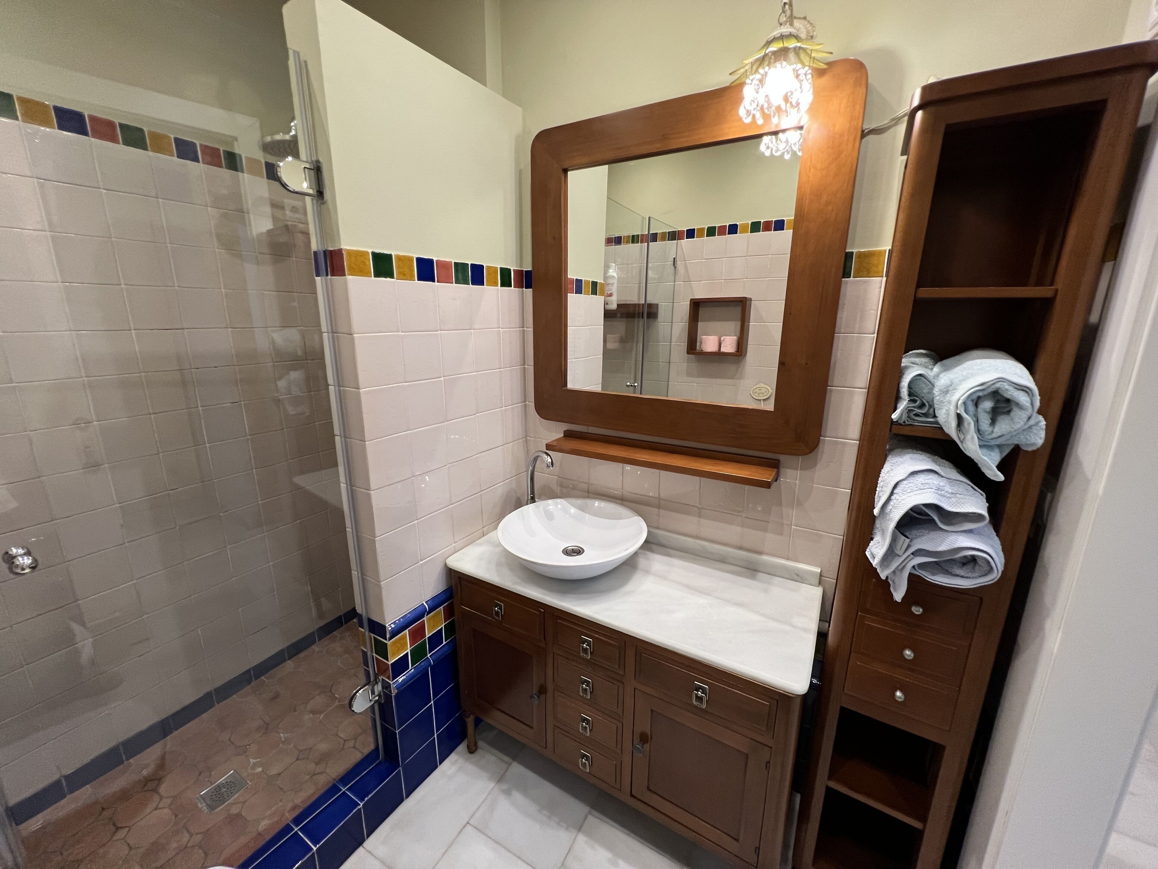 Une salle de bain avec un lavabo blanc, des meubles en bois, un miroir et une douche.