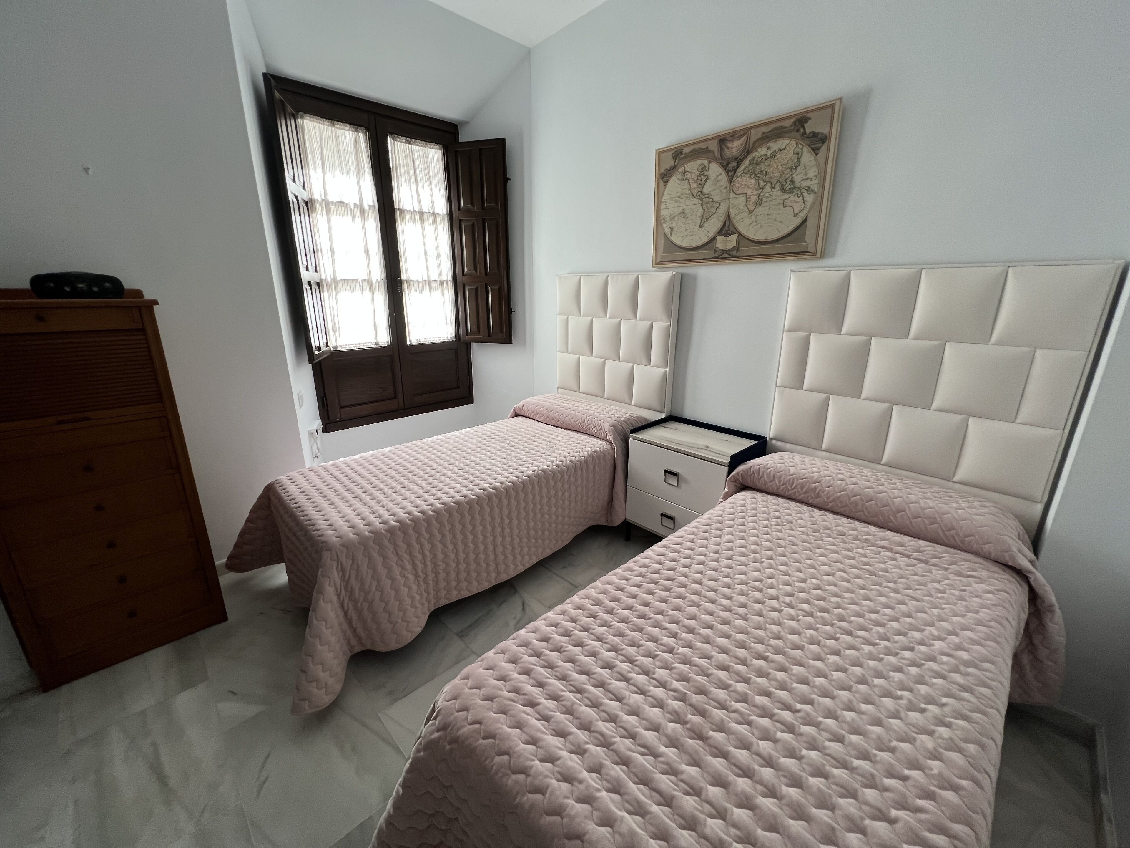 Un dormitorio con dos camas, un aparador, una ventana con cortinas y un globo terráqueo fijado a la pared.