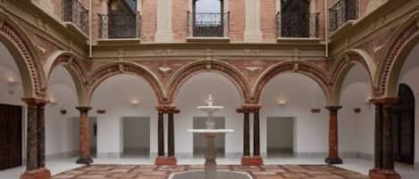 A courtyard with a central fountain, surrounded by arches and columns, and a balcony on the upper level.