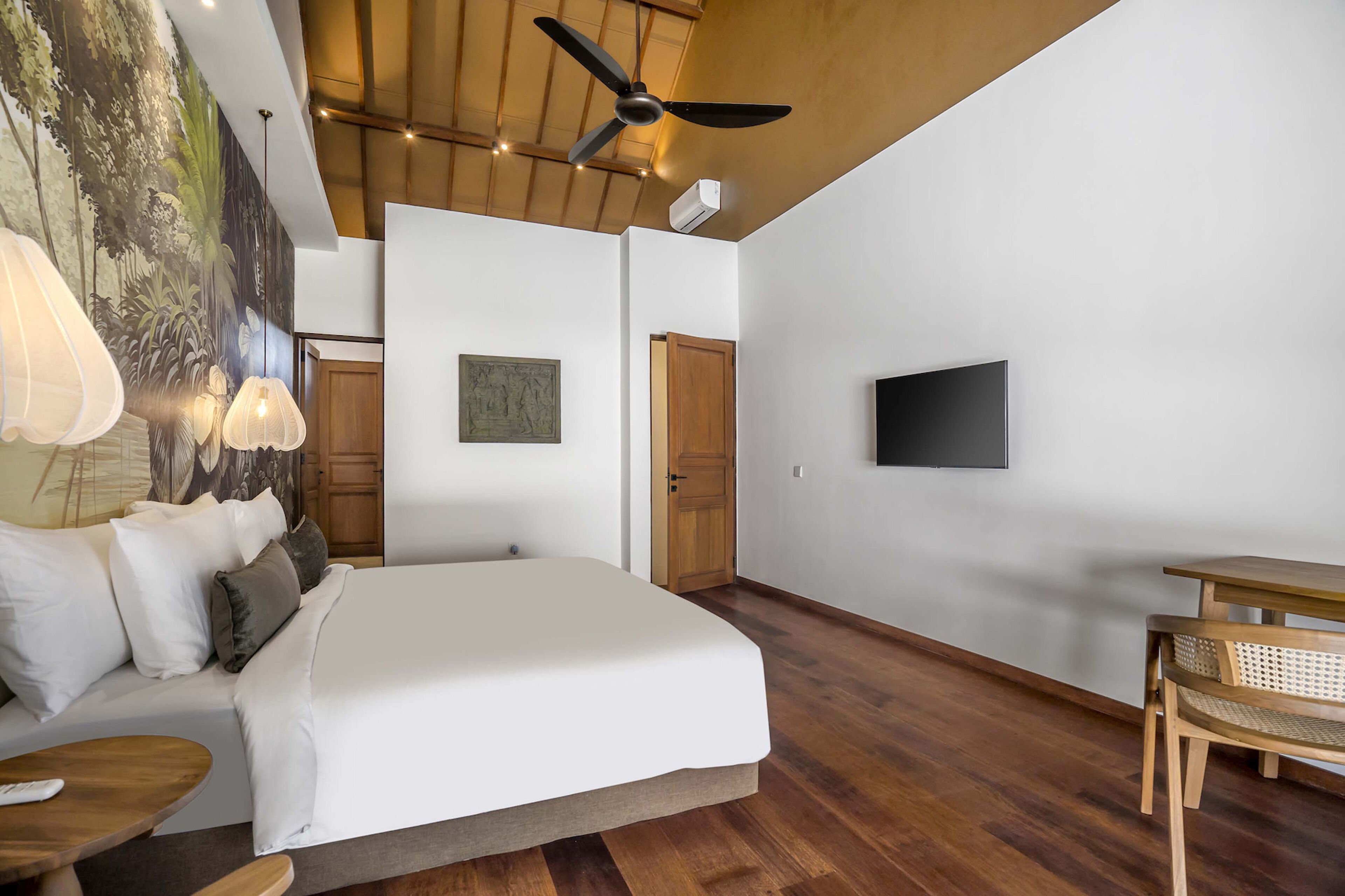 Un dormitorio con cama, ventilador de techo, televisor y zona de comedor con mesa y silla.