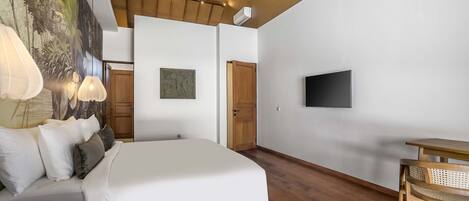 Un dormitorio con cama, ventilador de techo, televisor y zona de comedor con mesa y silla.