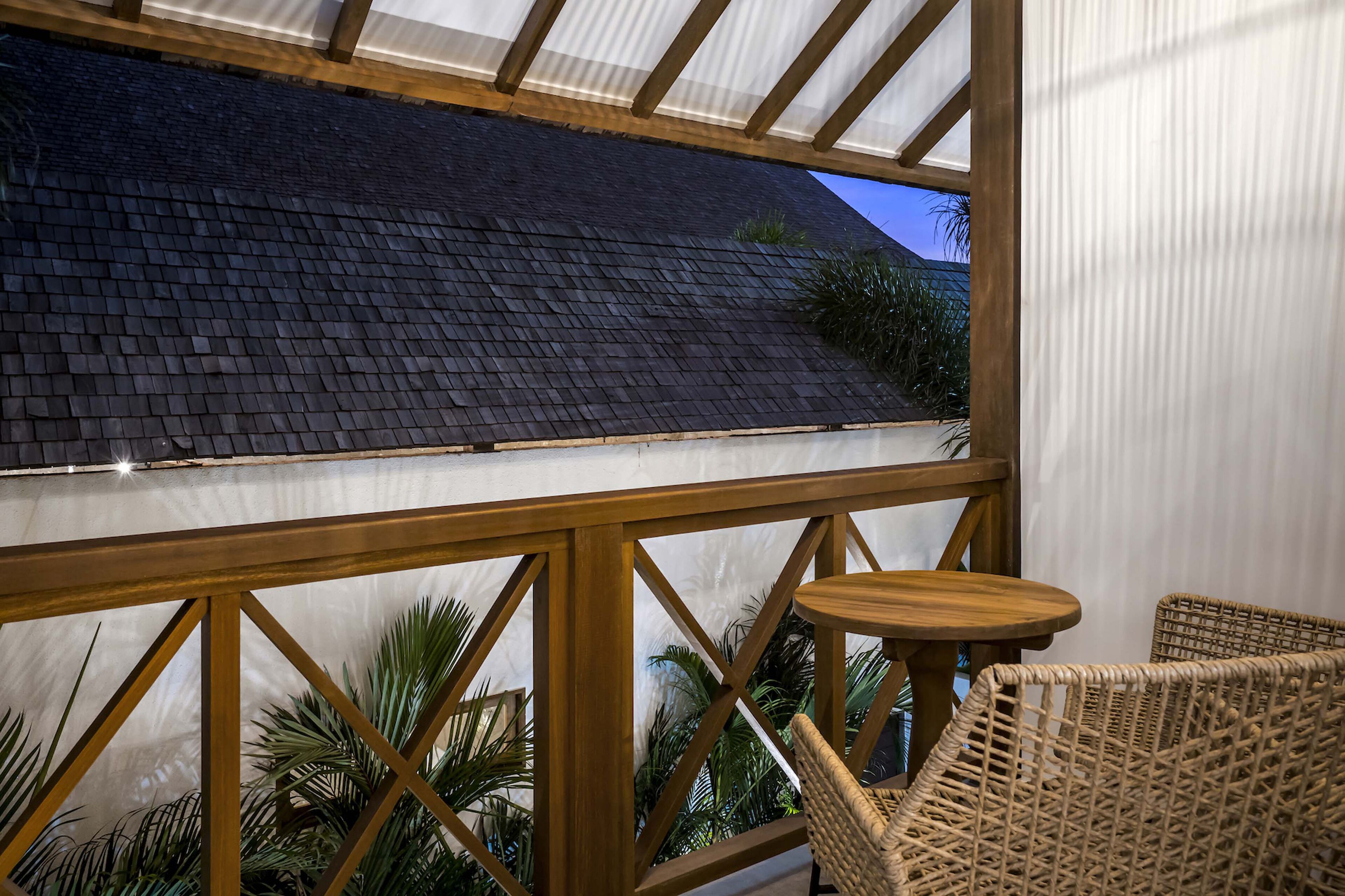 A balcony with a view of a dark roof, wooden railings, and wicker furniture.