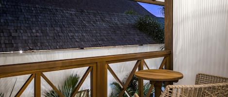 Een balkon met uitzicht op een donker dak, houten leuningen en rieten meubilair.