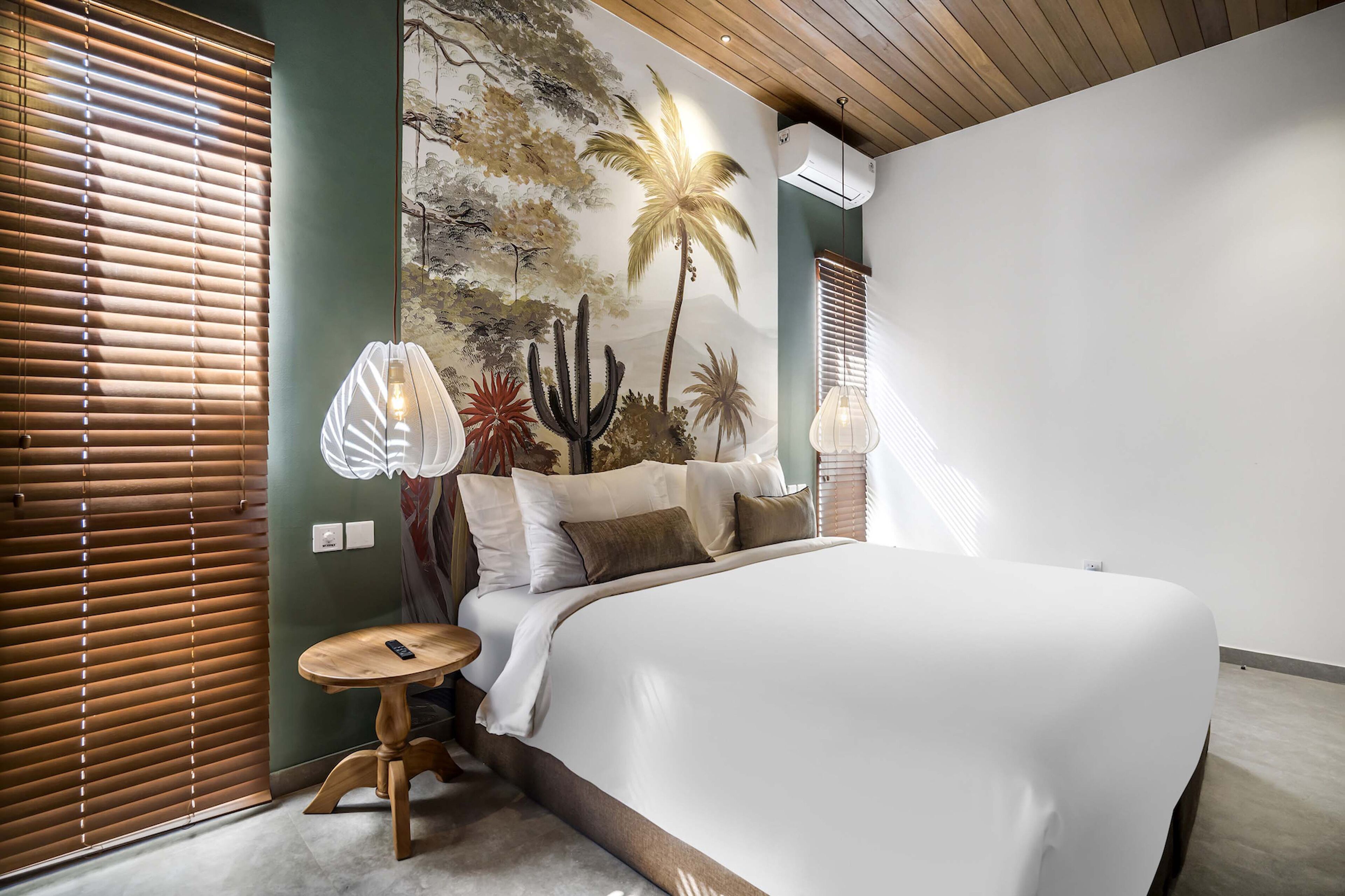 A bedroom with a large bed, a wall mural, a round wooden table, and a lamp.
