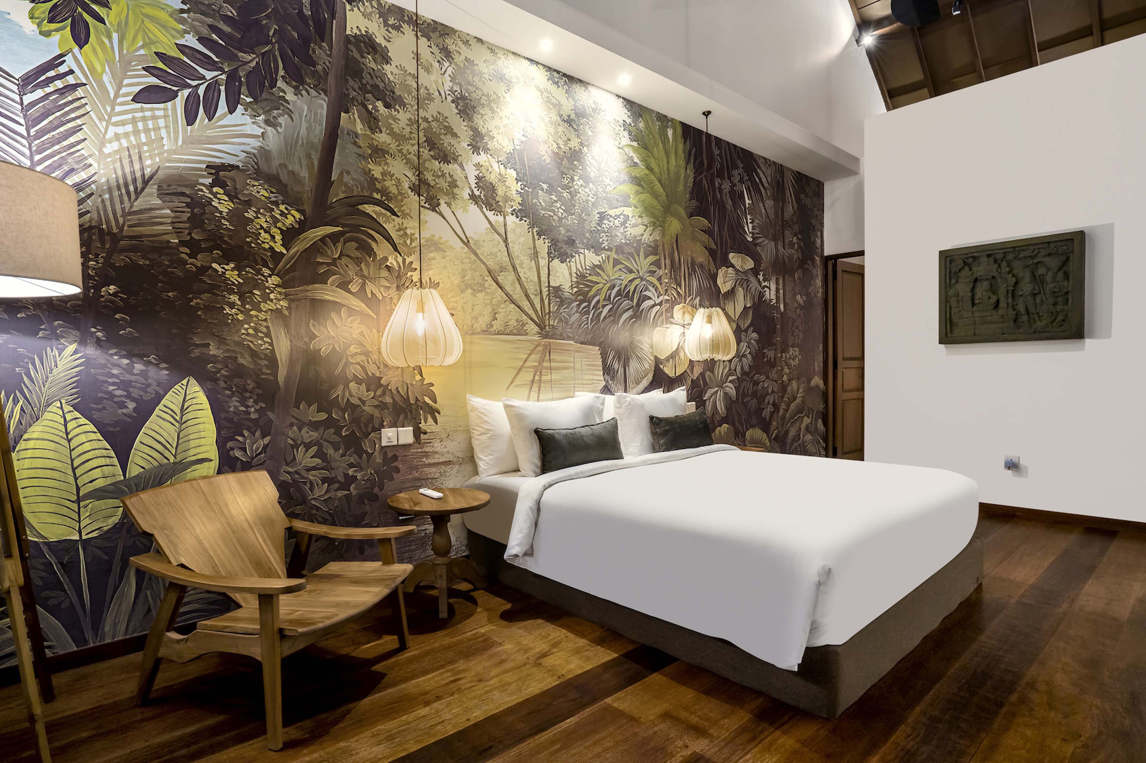 A bedroom with a large bed, a chair, a small table, and a mural on the wall.
