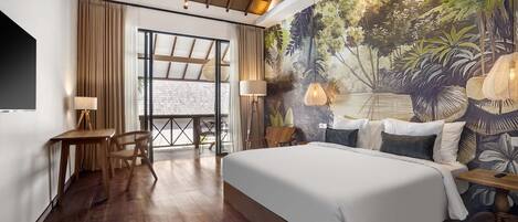 A bedroom with a large bed, wooden floor, a desk with a chair, a table, and a mural of a tropical scene.