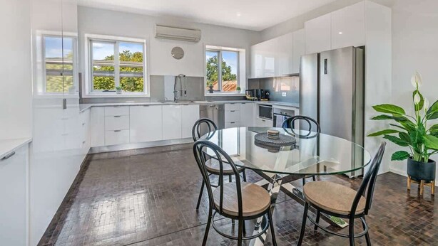 A modern kitchen with white cabinets, a stainless steel refrigerator, and a glass dining table with four chairs. - Bayne St Studio (Bendigo)