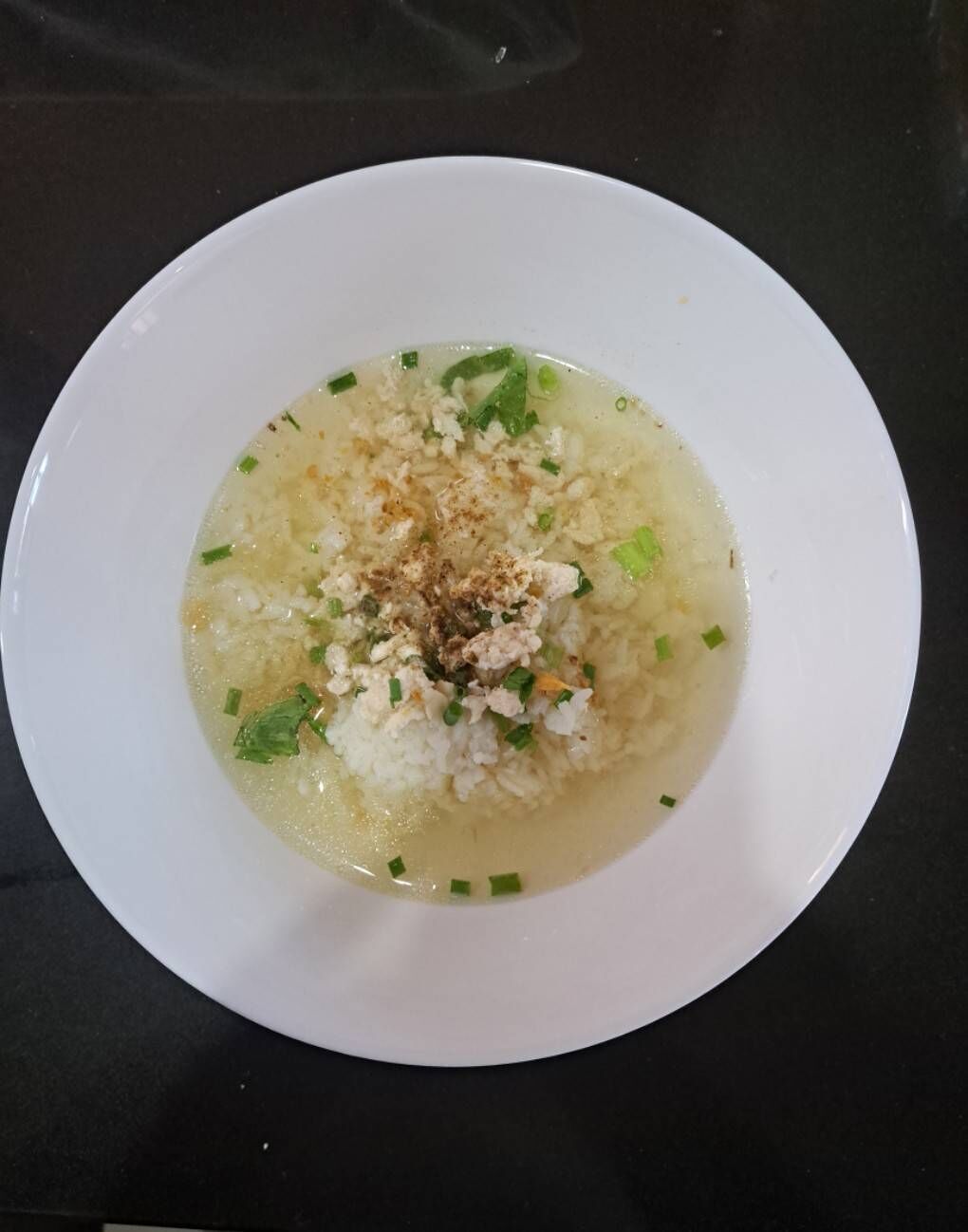 Un plato blanco con sopa transparente, adornado con cebollín picado y una pizca de condimento.