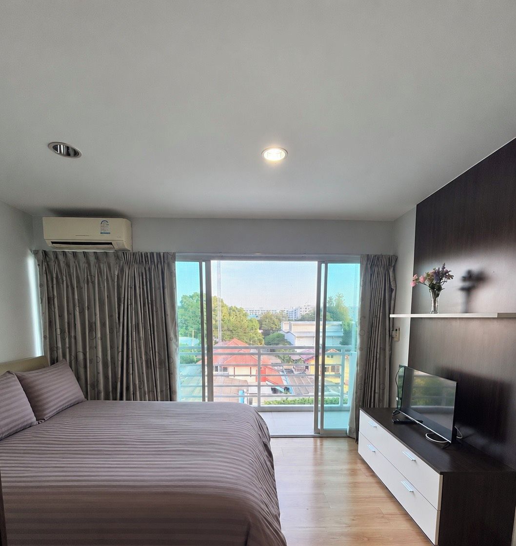 A modern bedroom with a large bed, a flat-screen TV, and a sliding glass door leading to a balcony.