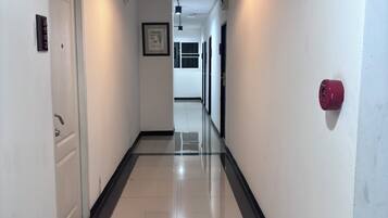 A corridor with a white door, a framed picture on the wall, and a red fire alarm on the right.