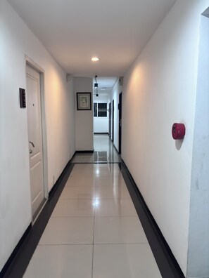 Un couloir avec une porte blanche, un tableau encadré au mur et un détecteur d’incendie rouge sur le côté droit.