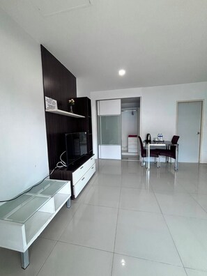 A modern hotel room with a flat-screen TV, a glass coffee table, a dining area with a table and chairs, and a walk-in closet. - BKK TEAK (Bangkok)