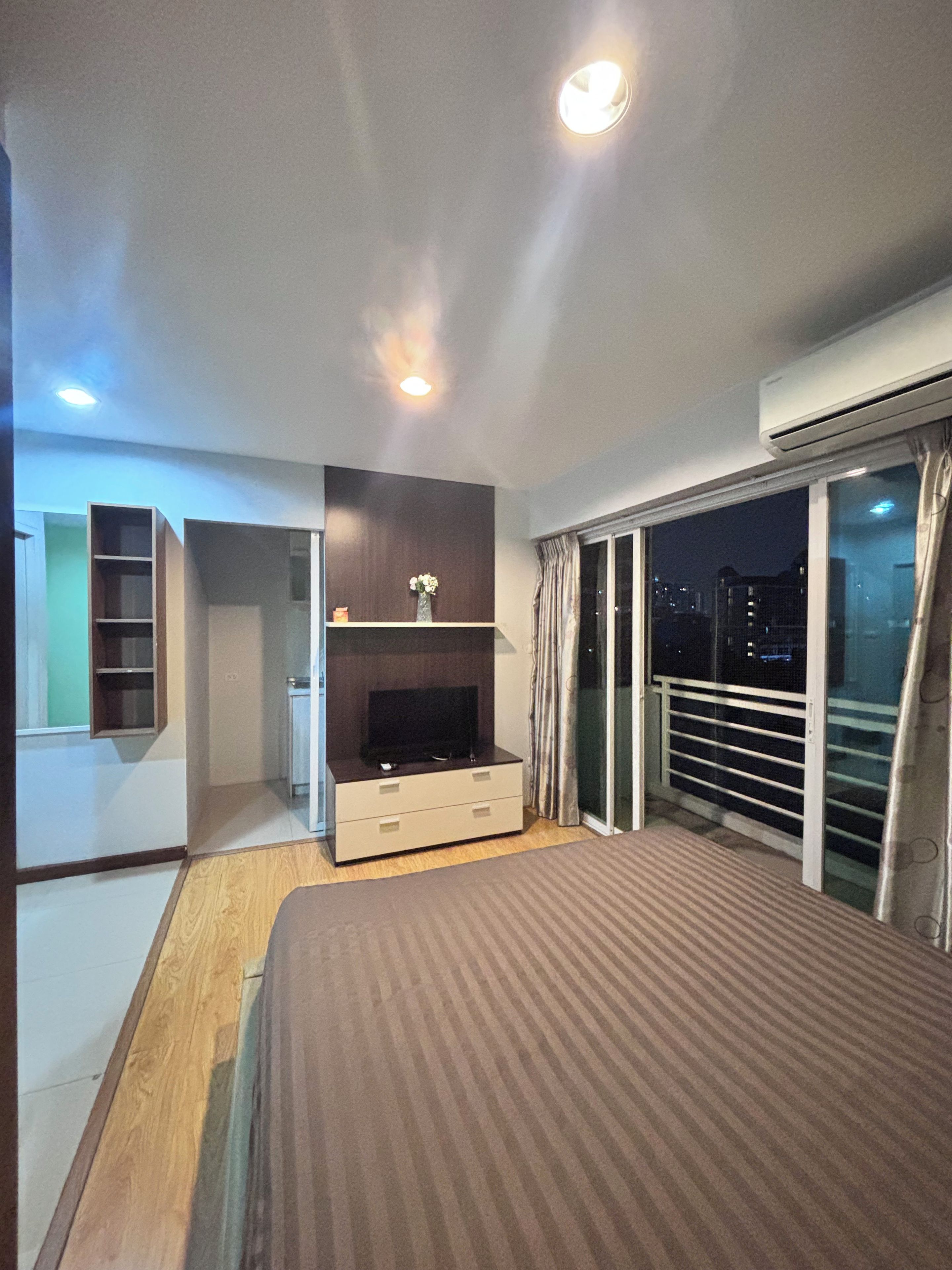 Een slaapkamer met een bed, een televisie, een klein kastje en een balkon met gordijnen.
