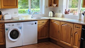 Une cuisine avec des meubles en bois, un lave-linge encastré, un évier et une fenêtre donnant sur un espace verdoyant.