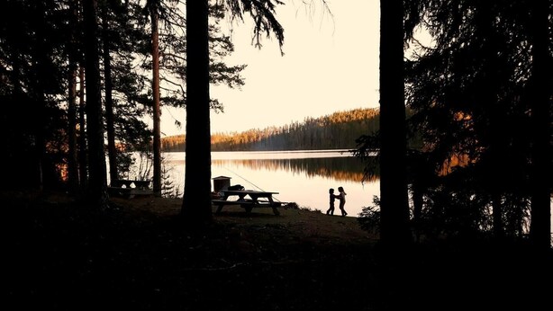 A lakeside scene with a picnic table and a small shed, surrounded by tall trees. - Cozy swedish house with fireplace & big garden (Ramsele)