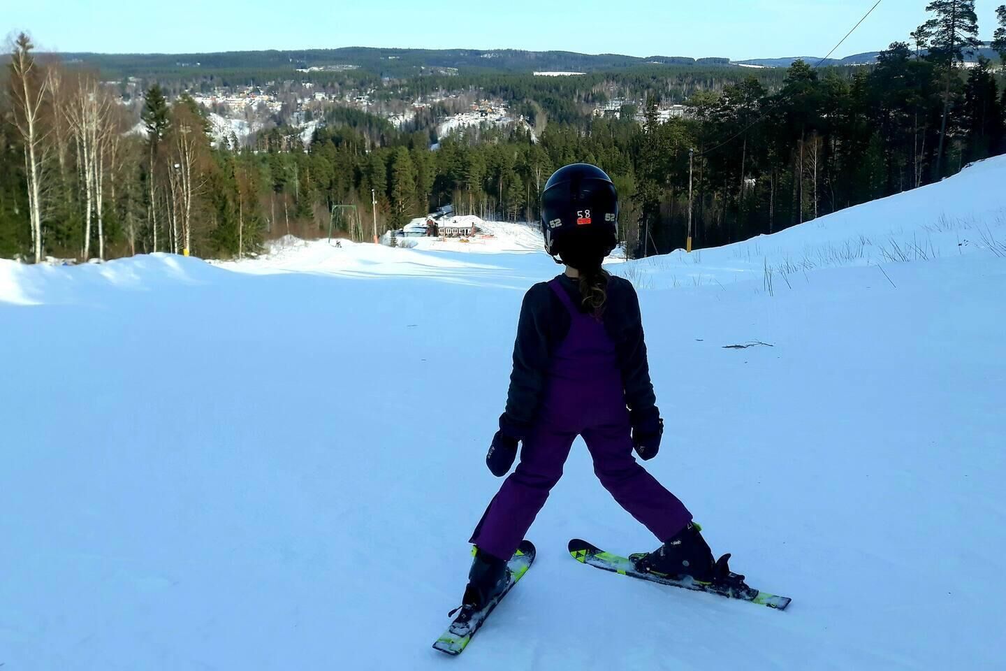 A child skiing on a snowy slope with a clear view of a town and forest in the background.