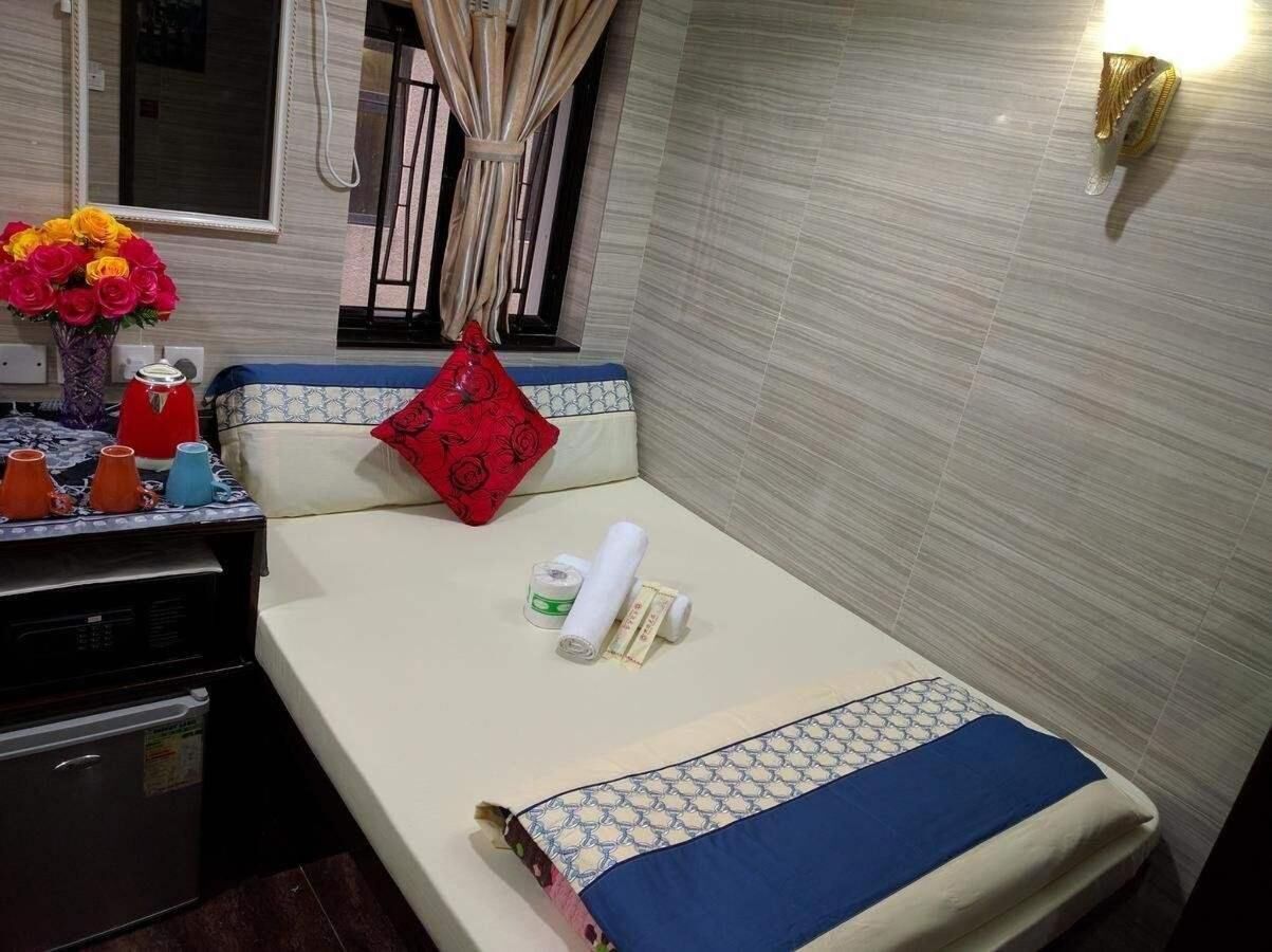 Una cama bien tendida con una colcha de cuadros azules y blancos, una almohada roja y un florero sobre la mesita de noche.