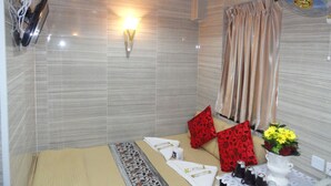 A hotel bathroom with a shower, a towel rack, a wall-mounted light, a fan, and a table with toiletries. - Davao Hostel (Kowloon)