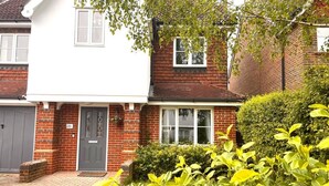 A two-story house with a brick facade, a grey door, and a small front garden with green shrubs. - Remarkable 5-Bed House in Horley (Horley)