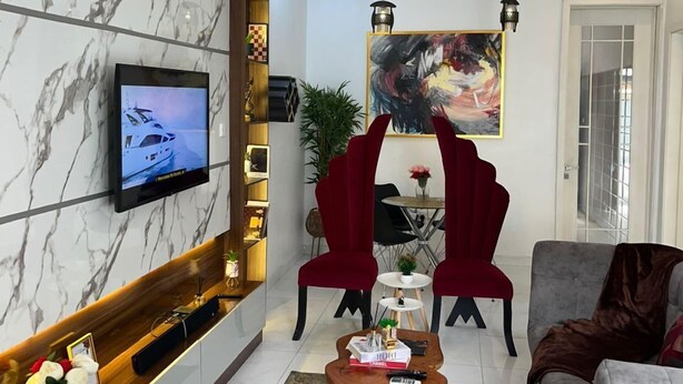 Un salon moderne avec un mur en marbre, un téléviseur à écran plat, des fauteuils rouges, un canapé gris et un tableau.