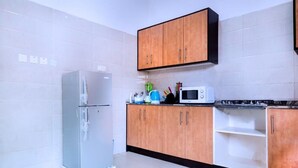 Une cuisine avec des murs recouverts de carreaux blancs, un réfrigérateur en acier inoxydable, des meubles de cuisine en bois, un four à micro-ondes et un plan de travail sur lequel se trouvent divers objets.