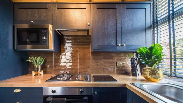 A modern kitchen with dark wood cabinets, a stainless steel microwave, a gas stove, and a window with blinds.