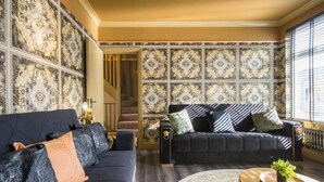 A living room with a dark blue sofa, a matching armchair, and a patterned wall. A staircase is visible in the background.