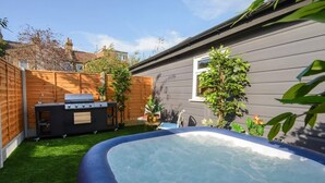 A backyard with a hot tub, barbecue grill, and a small pool.