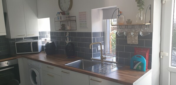 Una cocina equipada con microondas, lavadora, pileta y diferentes utensilios de cocina.