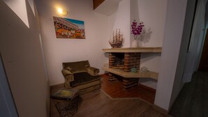 Quarto acolhedor com piso de madeira, sofá de couro marrom, uma pequena mesa com um livro, um modelo de navio em uma prateleira e um vaso com flores.
