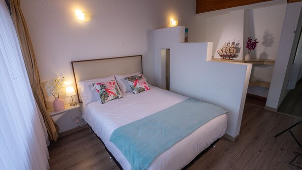 Quarto com cama, luminárias de cabeceira, mesa de cabeceira, modelo de navio decorativo e um vaso com flores.