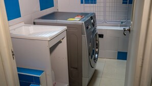 Uma lavanderia compacta com máquina de lavar e secadora, uma pequena prateleira e piso revestido de azulejos.