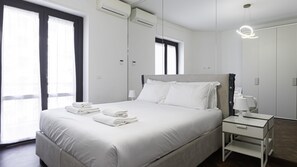 Quarto de hotel moderno com uma cama grande, uma mesa de cabeceira com abajur e um guarda-roupa.
