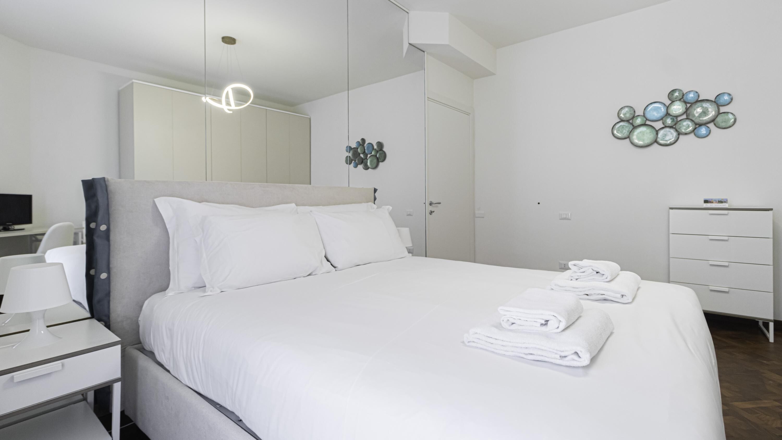 Una habitación de hotel moderna con una cama grande, un escritorio con lámpara, un armario y un adorno en la pared.
