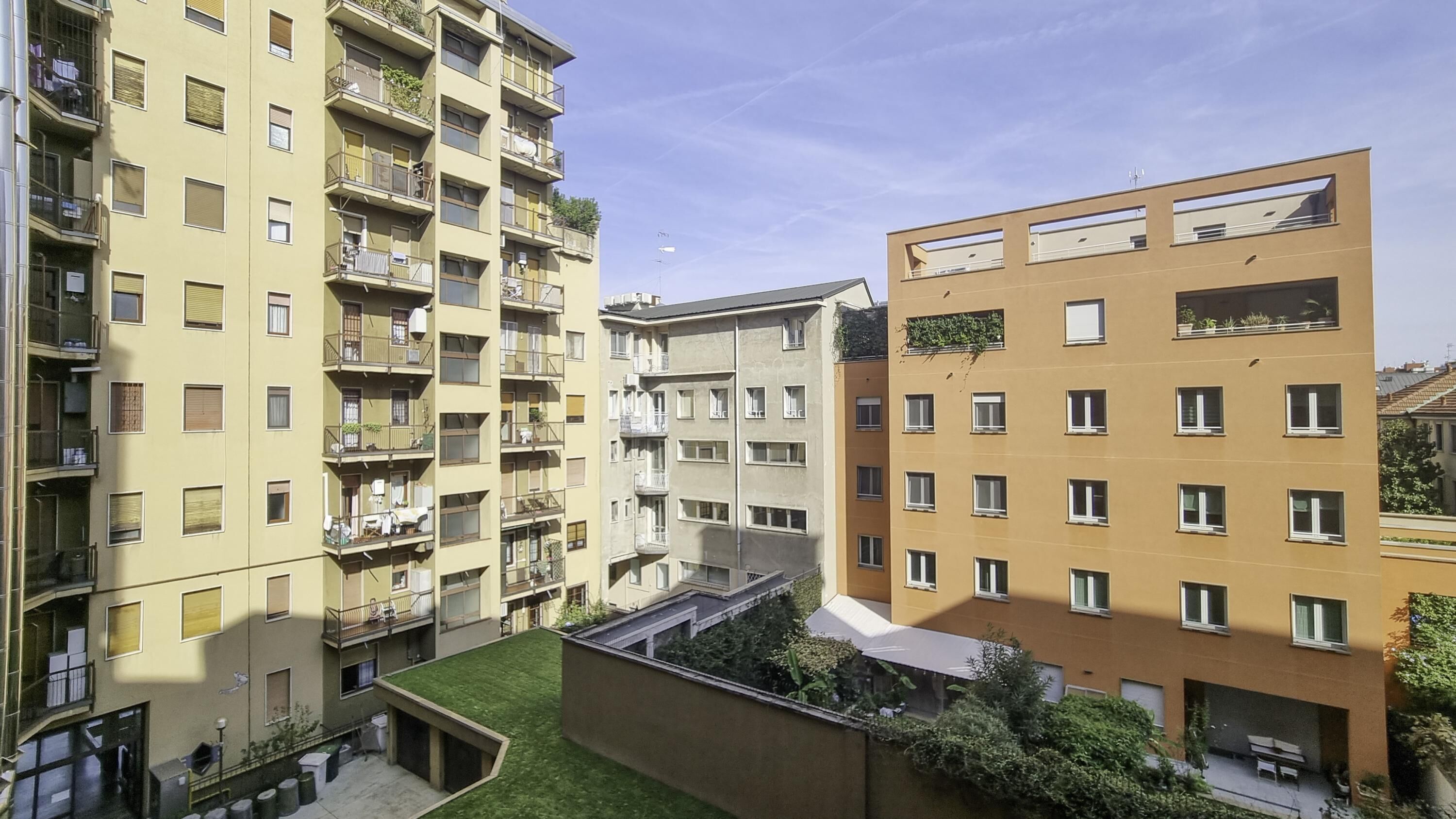 A multi-story residential building with balconies, a courtyard, and a small garden area.