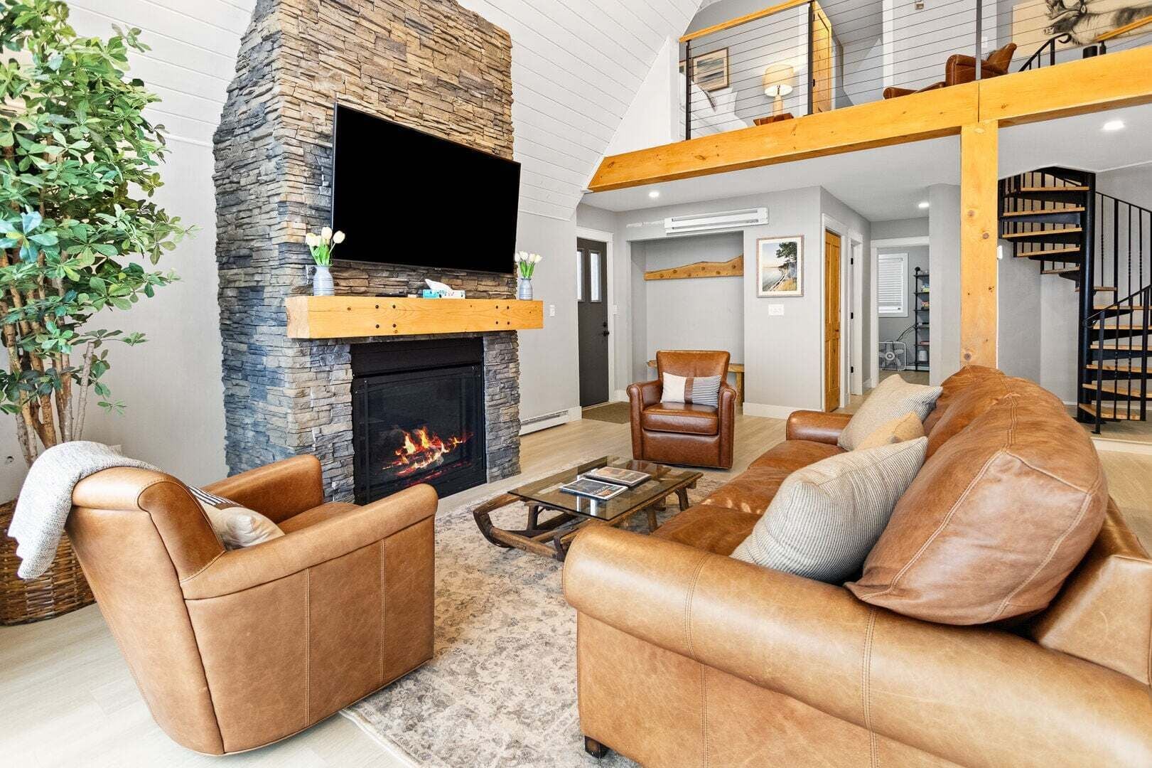 A living room with a stone fireplace, leather sofas, a coffee table, and a staircase leading to an upper level.
