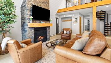 A living room with a stone fireplace, leather sofas, a coffee table, and a staircase leading to an upper level.