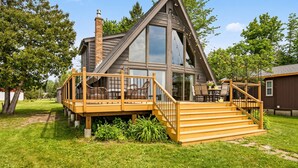 A modern house with a large deck, a chimney, and a staircase leading to the entrance. - Caribou Lake A-Frame w/ Sauna, Heirloom Vacations (Duluth)
