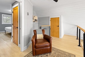 A room with a brown leather chair, a wooden door, a white wall, and a window.