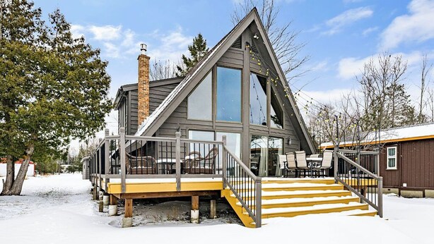A modern cabin with a steeply pitched roof, large windows, and a wooden deck with outdoor seating. - Caribou Lake A-Frame w/ Sauna, Heirloom Vacations (Duluth)