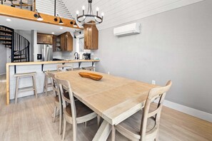 Une cuisine moderne avec des meubles en bois, une cuisinière encastrée et un coin repas comprenant une table et des chaises en bois.