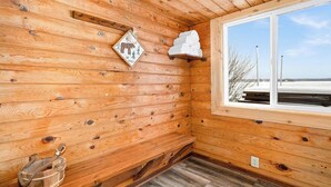 A wooden cabin interior with a window, a wall-mounted heater, and a wooden bench. - Caribou Lake A-Frame w/ Sauna, Heirloom Vacations (Duluth)
