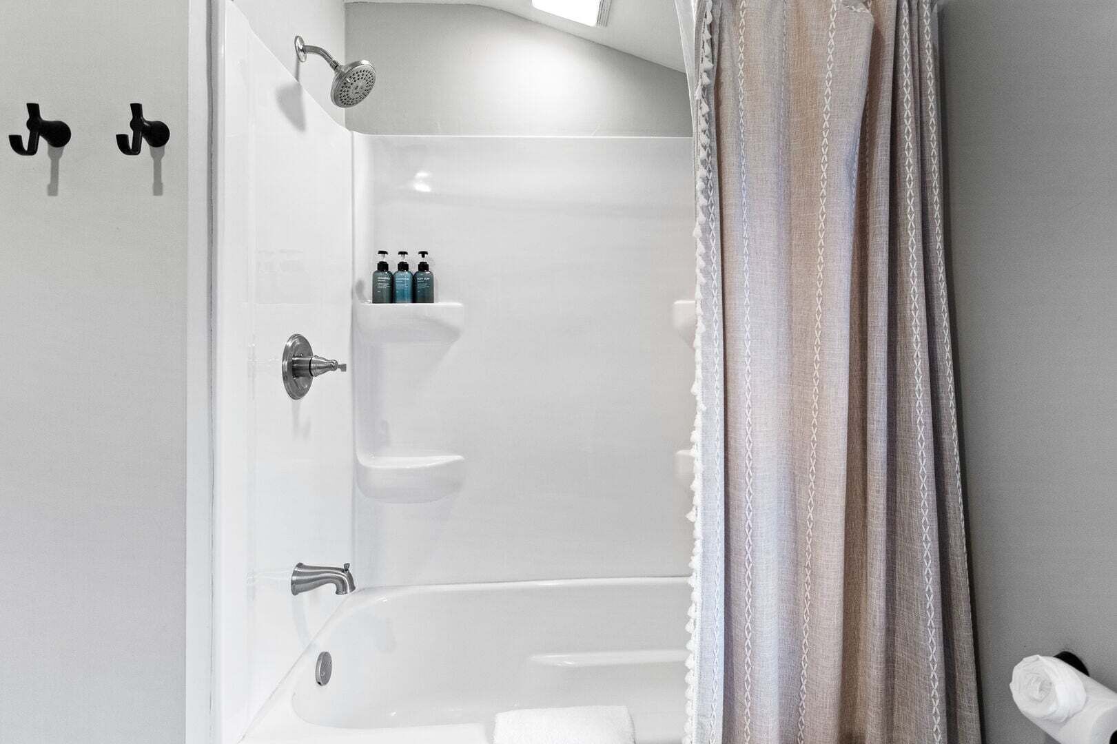 A bathroom with a bathtub, a shower, and a toilet. There are toiletries on the wall and a towel on the floor.