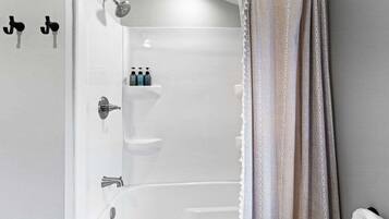 A bathroom with a bathtub, a shower, and a toilet. There are toiletries on the wall and a towel on the floor.